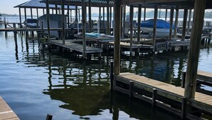 A wooden dock extending into calm water, with a covered structure in the background. - Beautiful False River Home on water w/ Dock (New Roads)