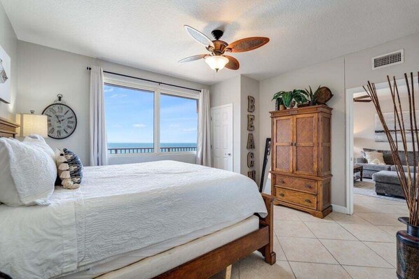 Un dormitorio con cama, ventilador de techo, un armario de madera y un ventanal con vistas.