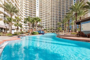 Una amplia piscina interior con palmeras y sillas de descanso, rodeada de altos edificios de hotel.