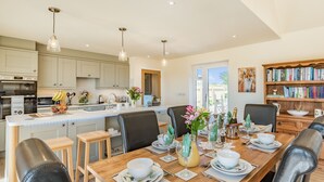 A spacious kitchen with modern appliances, a dining area with a wooden table set for six, and a bookshelf filled with books.