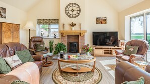 A cozy living room with leather sofas, a fireplace, a television, and a large window.