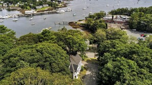 Vista aérea de uma cidade costeira com um porto cheio de barcos, cercada por vegetação densa e edifícios residenciais.