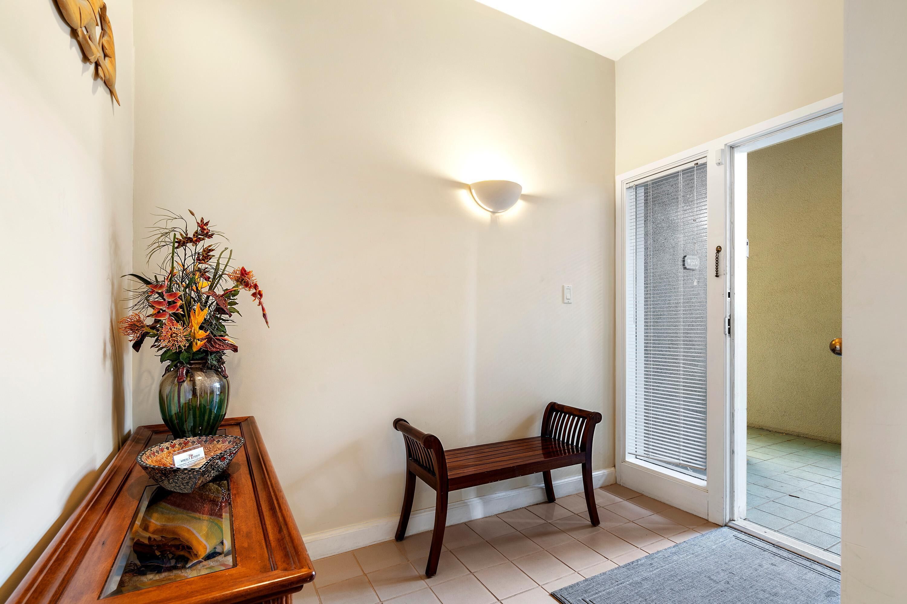 Un couloir avec un banc en bois, un vase rempli de fleurs et un luminaire fixé au mur.
