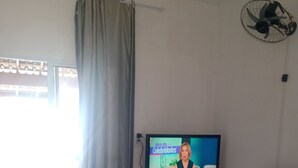 Ett vardagsrum med en tv-apparat som visar ett nyhetsprogram, en blå soffa, en vit tv-möbel och en skjutdörr i glas med gardiner.