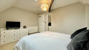 A bedroom with a bed, a dresser, a television, a ceiling light, and a door. - 2 bedroom accommodation in Cirencester (Cirencester)