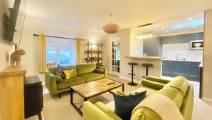 A modern living room with a green sofa set, a wooden coffee table, and a TV mounted on the wall. - 2 bedroom accommodation in Cirencester (Cirencester)
