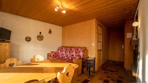 A wooden interior with a dining table, chairs, a sofa, and a television. - Small apartment on the ski slopes (Gryon)
