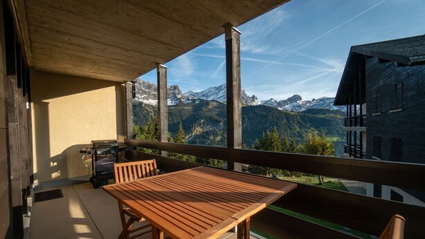 A balcony with a wooden table and chairs, overlooking a mountainous landscape. - Small apartment on the ski slopes (Gryon)