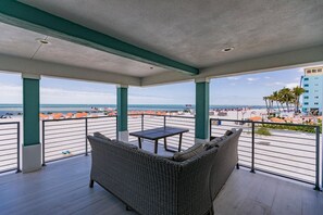 A balcony with a wicker sofa and a small table, overlooking a beach with umbrellas and palm trees. - Sand Dollar North - Beachfront View (Fort Myers Beach)