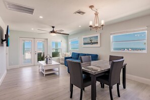 A modern living room with a dining area, a ceiling fan, and a view of the ocean.