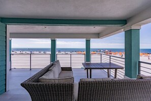 A covered outdoor seating area with wicker furniture and a view of the beach.
