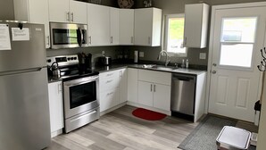A modern kitchen with stainless steel appliances, white cabinets, and a red rug. -  Quiet countryside shipping container home. Relax or enjoy outdoor recreation  (Westby)