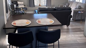 A modern living room with a dark brown dining table, two black chairs, a grey sofa, and a black leather chair. -  Quiet countryside shipping container home. Relax or enjoy outdoor recreation  (Westby)