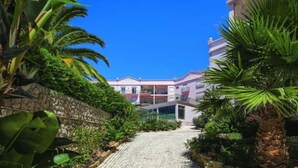 A pathway leading to a building with a stone wall on one side and lush greenery on the other. - Casa Da luz 5, ocean view, pool & beach 200 meters away  (Praia da Luz)