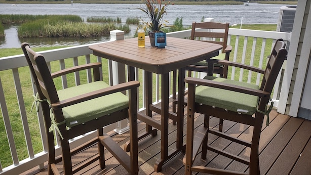 A wooden deck with a table and chairs, overlooking a body of water and a forested area.