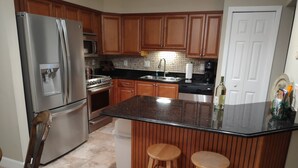 A kitchen with wooden cabinets, stainless steel appliances, a granite countertop, and two wooden stools.