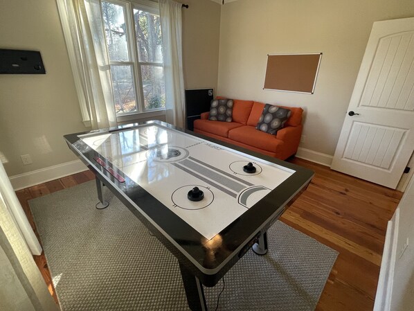 A room with a foosball table, a sofa, a door, and a window.