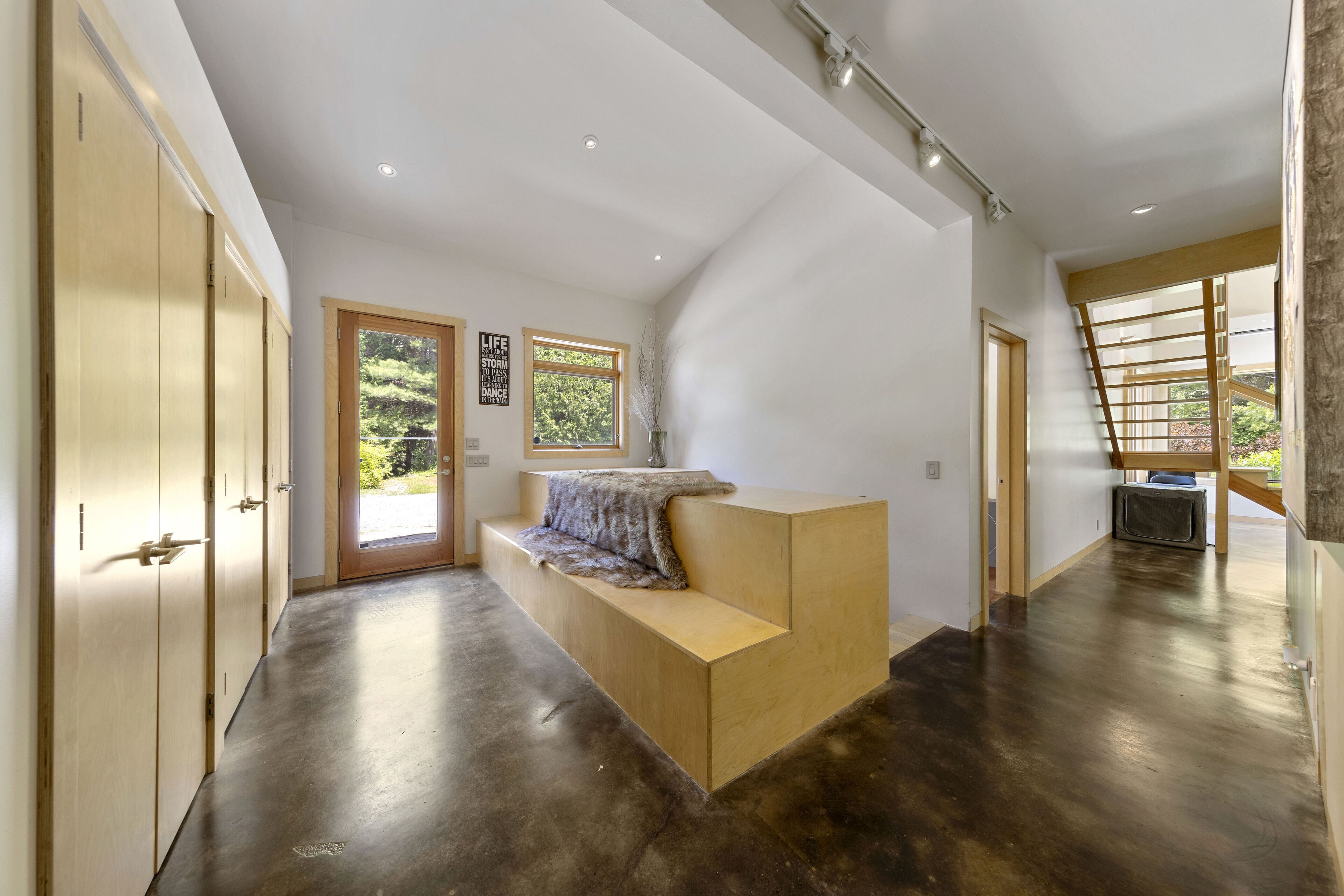 Un interior moderno con un banco de madera, una escalera y vistas a zonas verdes al exterior.