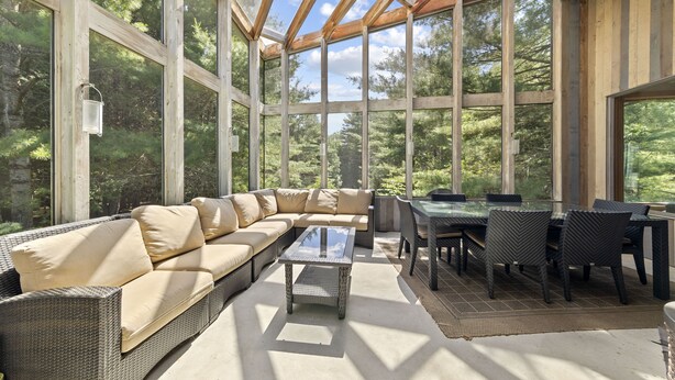 Un solarium con un amplio techo de cristal, un sofá modular, una mesa de comedor con sillas y una pequeña mesa de centro.