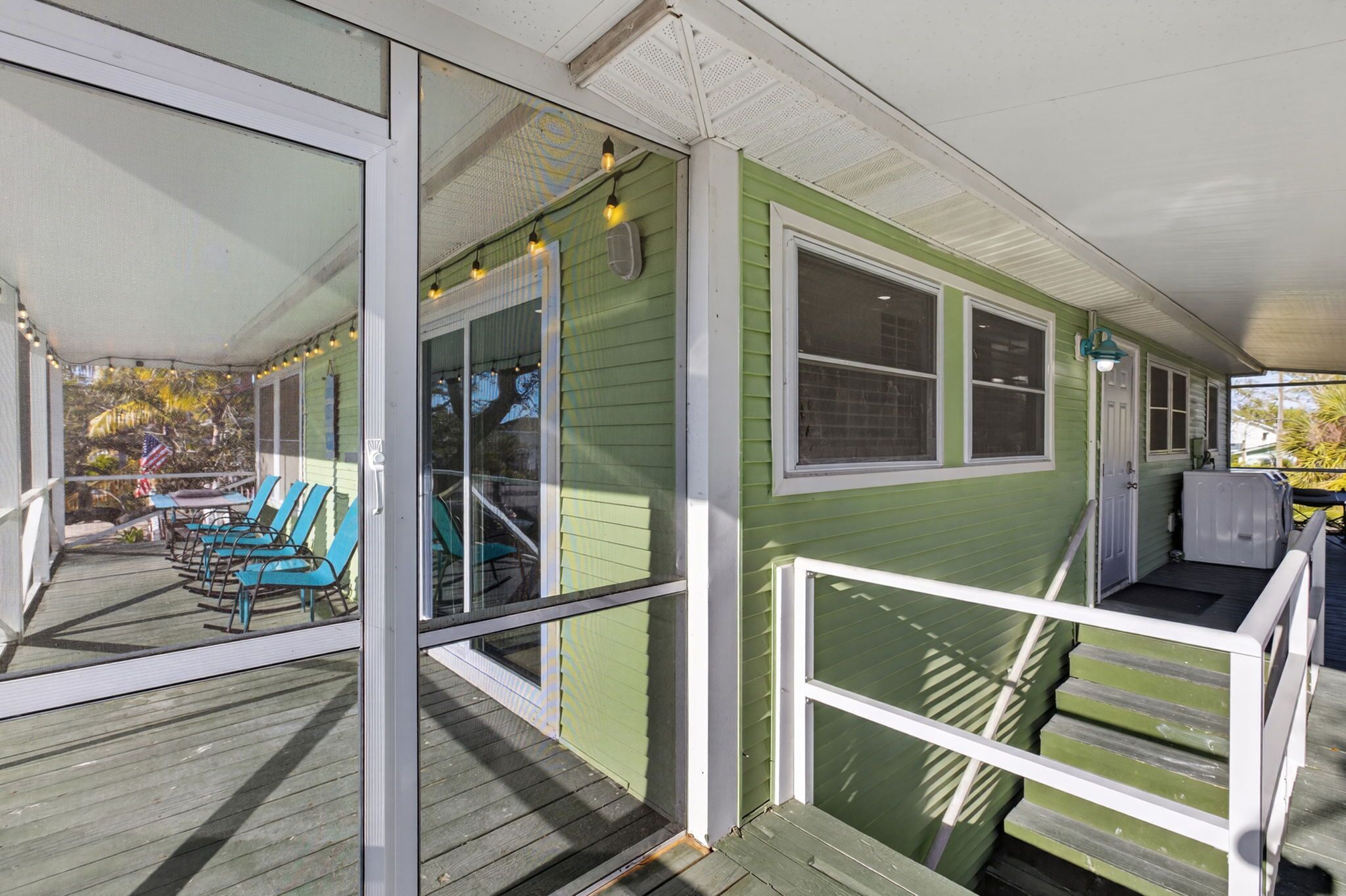 A green house with a porch, outdoor seating, and a covered area with steps.