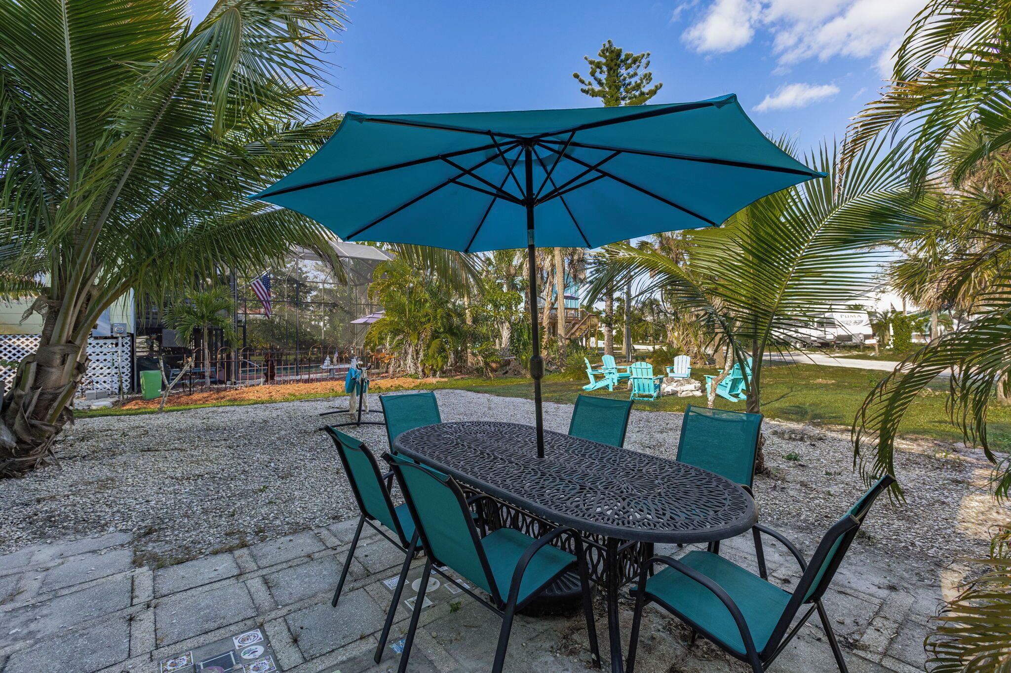 Une terrasse extérieure avec une table ronde et des chaises, un parasol bleu et des palmiers.