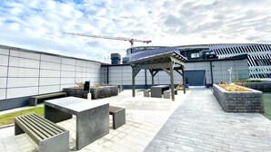 An outdoor patio area with concrete benches and planters, a pergola, and a modern building with a sloped roof in the background. - City Home Finland Arena Studio (Tampere)