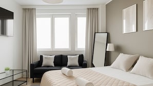 A modern hotel room with a large bed, a black sofa, a flat-screen TV, and a large window with curtains. - City Home Finland Arena Studio (Tampere)
