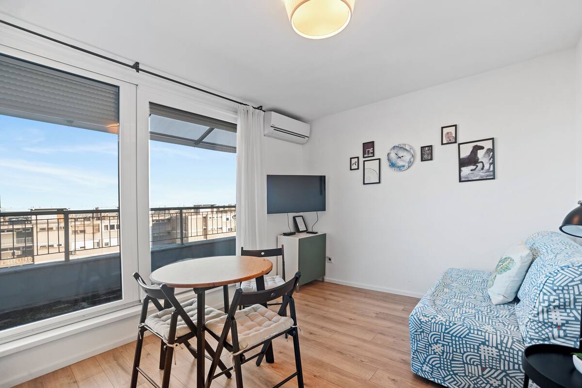 A modern living room with a dining area, large windows, and a city view.