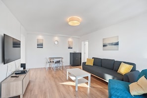 A modern living room with a flat-screen TV, a sofa, a coffee table, and a dining area with chairs and a cabinet. - Prime View Apartment Zagreb (Zagreb)