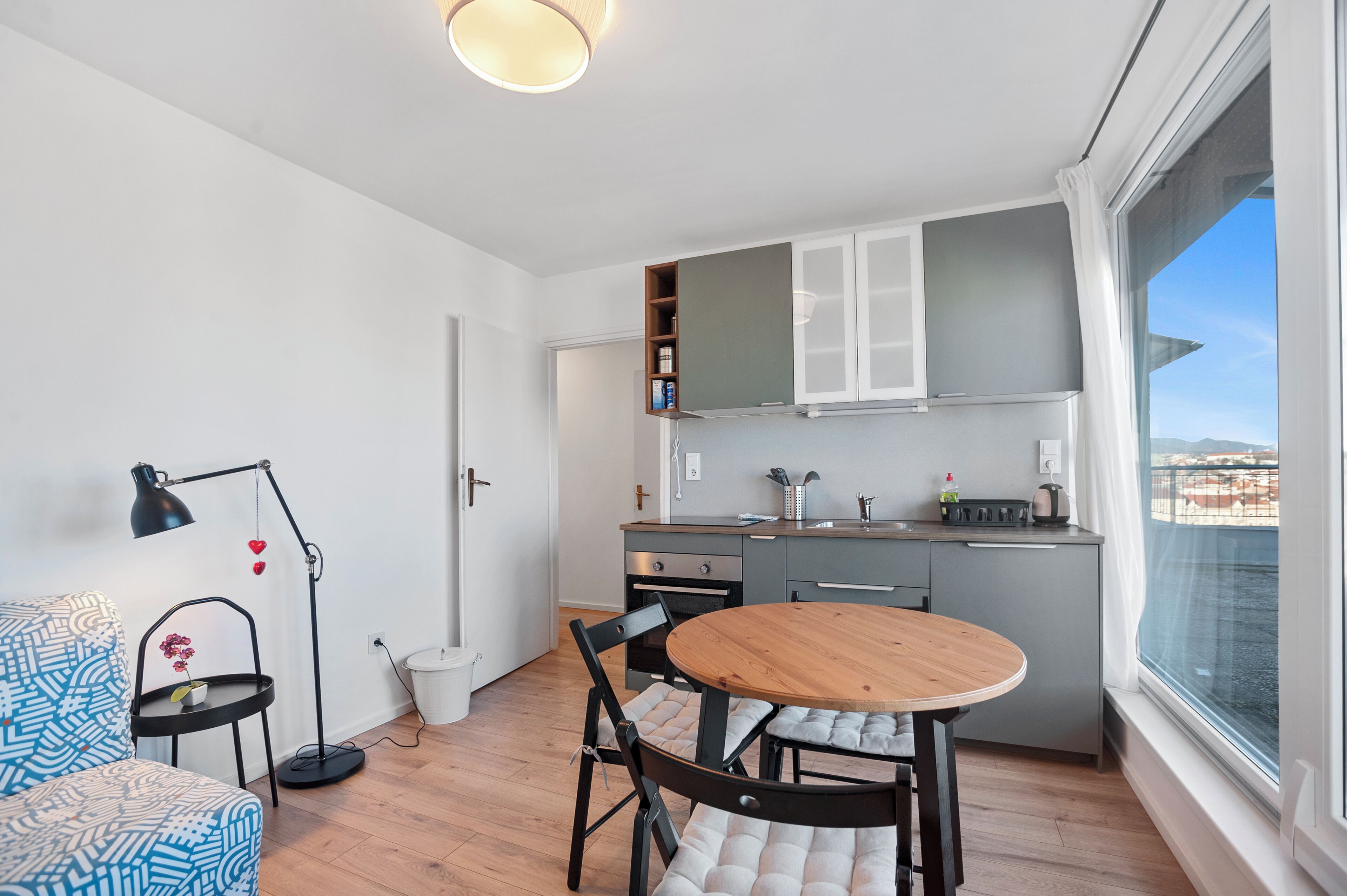 Une cuisine compacte avec un coin repas, une petite table d’appoint et une vue dégagée sur l’extérieur grâce à une grande fenêtre.