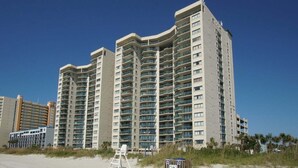 Een hoog hotel met meerdere balkons, gelegen nabij een strand met een redderspost en een strandbord.