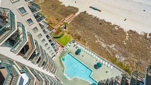 Een hoog hotel met een zwembad op het dak, uitzicht op het strand en een aangelegde tuin met een houten terras.