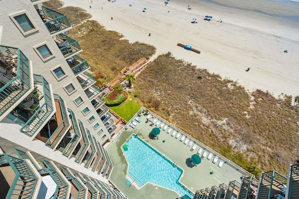Ein Hochhaus-Hotel mit Pool auf dem Dach, Blick auf den Strand und einer angelegten Grünfläche mit einer Holzterrasse.