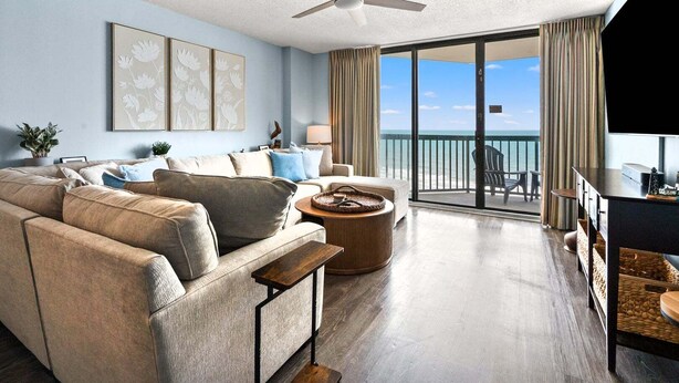 Een ruime woonkamer met een grote bank, een salontafel en een balkon met uitzicht op de oceaan.