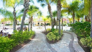 A paved pathway flanked by palm trees and greenery, leading to a building with a yellow facade. - Resort acess walking distance - Private pool (Kissimmee)