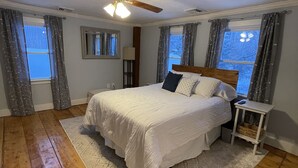 Une chambre à coucher avec un lit, un ventilateur de plafond, une table de chevet et une fenêtre avec des rideaux.