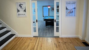 Un couloir doté d’un plancher en bois, d’une table de billard et de deux affiches accrochées aux murs.