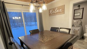 Un coin repas avec une table et des chaises en bois, un lustre et une vue sur un paysage enneigé, visible à travers de grandes fenêtres.