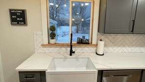 Une cuisine moderne dotée d’un grand îlot central, de meubles gris, d’un plan de travail blanc et d’une fenêtre donnant sur un paysage enneigé.