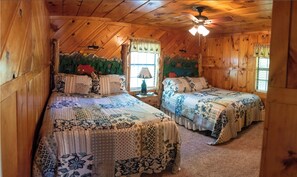 Une chambre confortable située dans les combles, avec deux lits, des murs en bois, un ventilateur de plafond et une fenêtre avec des rideaux.