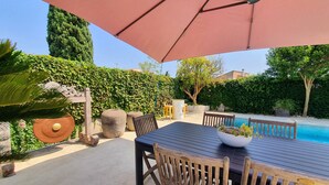 Un patio al aire libre con mesa y sillas, una piscina y un gran paraguas.