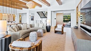 Amplia sala de estar con un sofá modular grande, una mesa de centro de madera y un sillón cómodo. Hay una chimenea, un televisor montado en la pared y una escalera que conduce a un nivel superior.