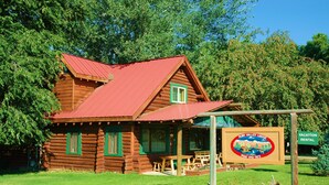 A rustic log cabin with a red roof, a porch with wooden benches, and a sign advertising Ruby Valley Lodge.
