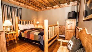 A wooden bedroom with a bed, two bedside tables, a nightstand, a wooden wardrobe, and a television.