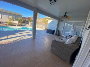 Un patio techado con piscina, mobiliario exterior y un ventilador de techo.