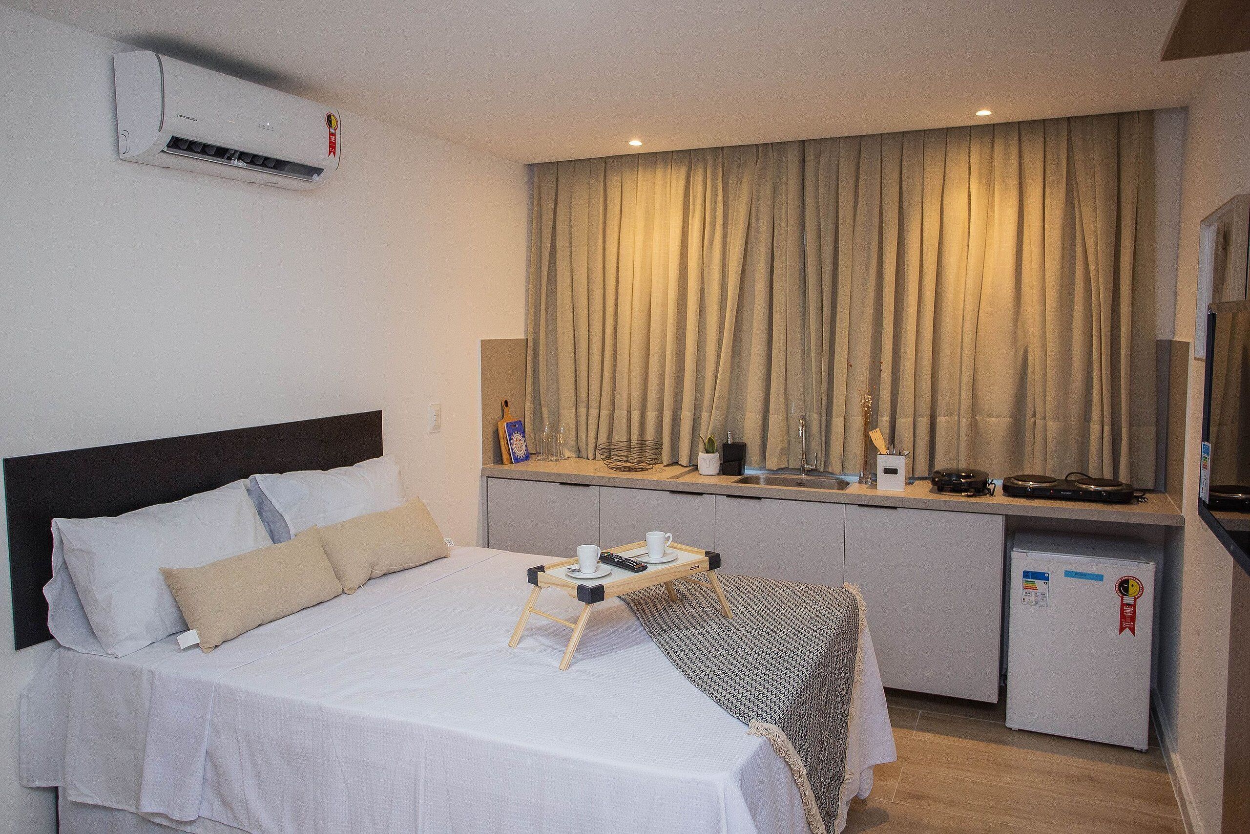 Une chambre d’hôtel de taille réduite, comprenant un lit, une table de chevet et un coin cuisine.