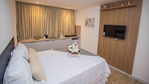 Habitación de hotel con cama, televisor montado en la pared, una mesita y una kitchenette.