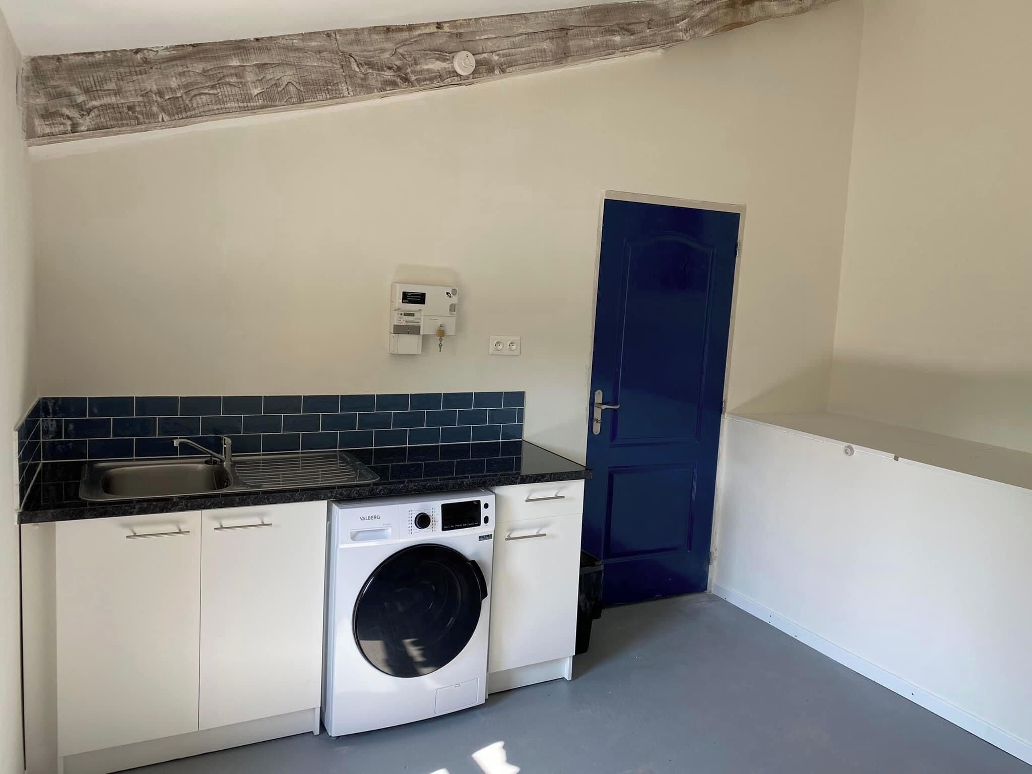 A compact kitchen with a washing machine, a sink, and a blue door.