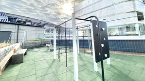 Ett utomhusgym med träningsredskap, ett grönt, gummibelagt golv och en byggnad med modern design i bakgrunden.