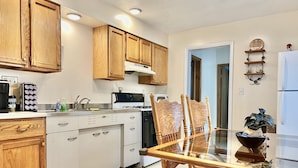 Una cocina moderna con armarios de madera, una estufa y un comedor con mesa y sillas de vidrio.